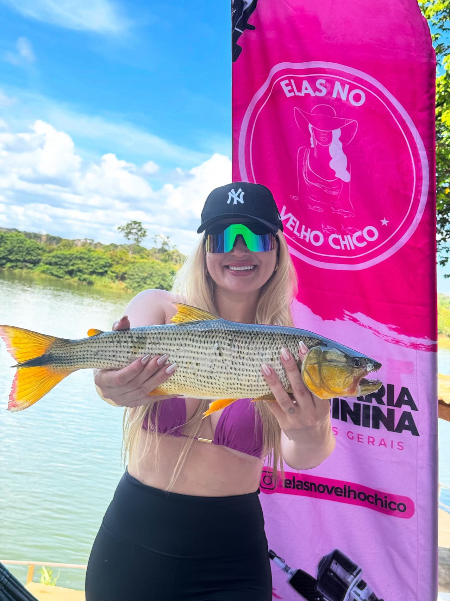Pescadora com tucunaré ao lado do banner Elas no Velho Chico